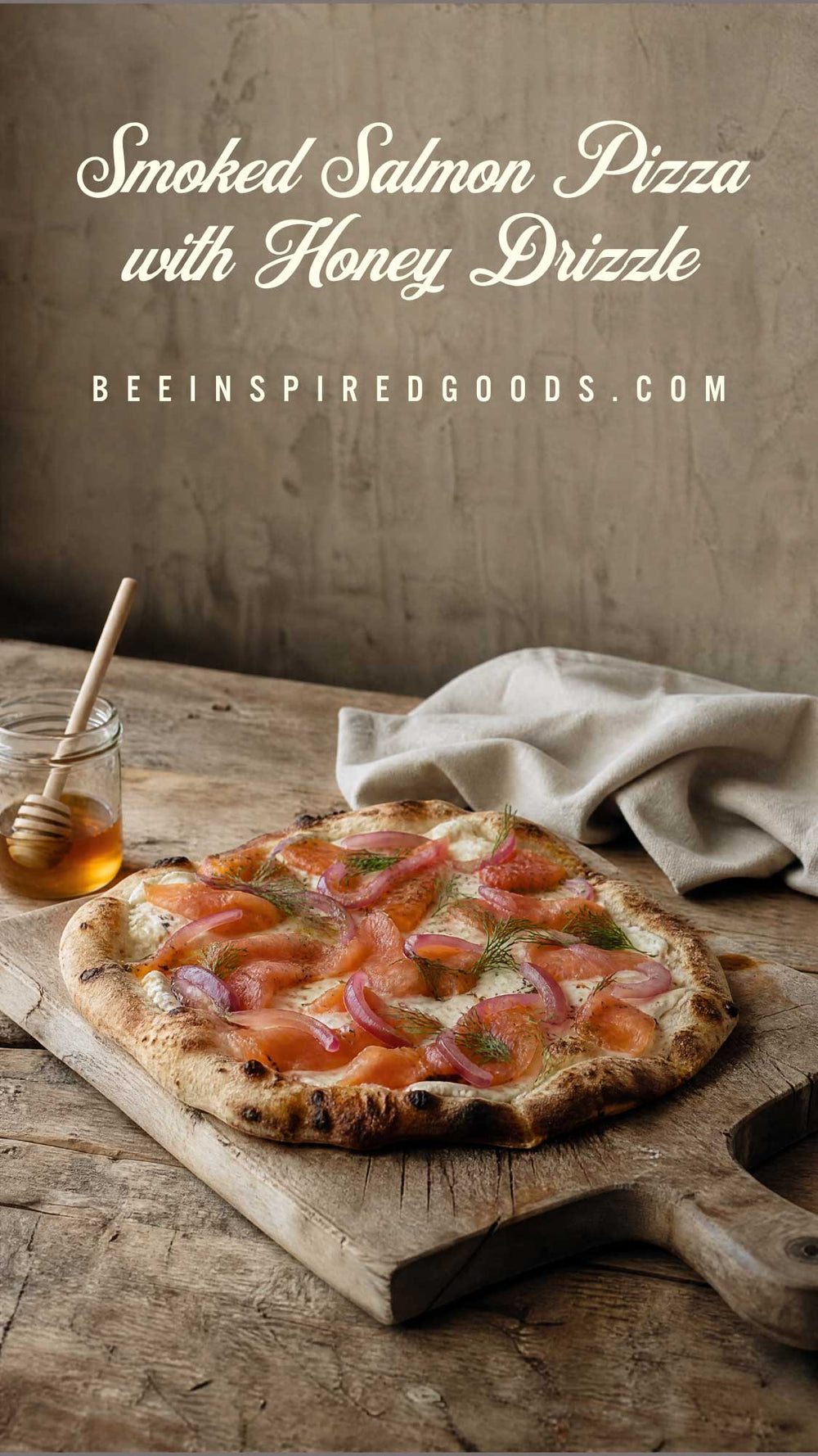 A smoked salmon pizza topped with honey drizzle, served on a rustic wooden board on a weathered table with a jar of honey and a cloth napkin. Text overlay reads 'Smoked Salmon Pizza with Honey Drizzle' and 'BEEINSPIREDGOODS.