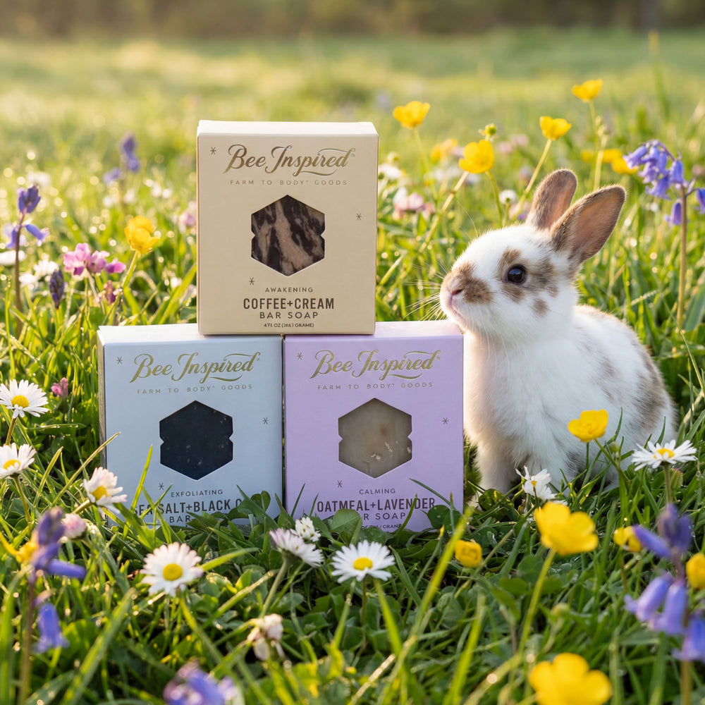 Three 'Bee Inspired' soap bars with their packaging on a grassy field with flowers and a rabbit.