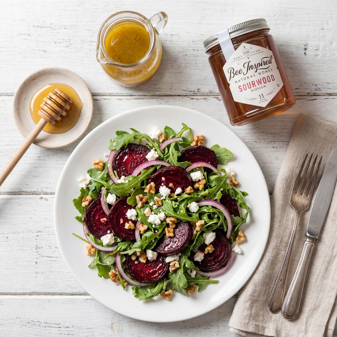 Salad with beets, greens, and nuts on a white plate with a jar of honey and a bottle of vinegar.