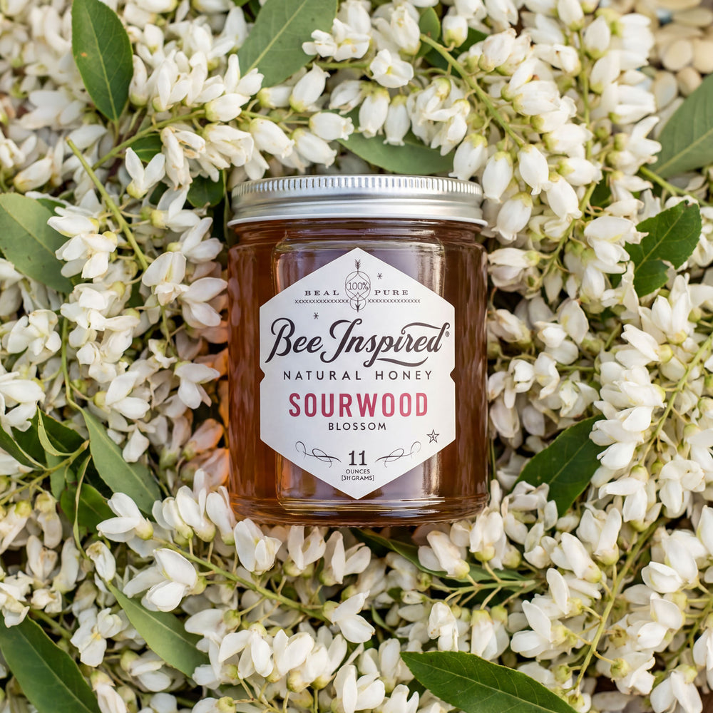 Jar of Bee Inspired natural honey surrounded by white flowers and green leaves