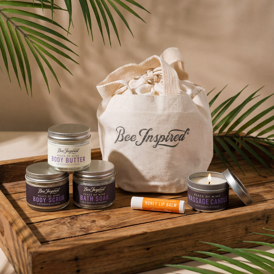 Collection of Bee Inspired beauty products including candles, lip balm, and body scrub on a wooden tray with a 'Bee Inspired' tote bag.
