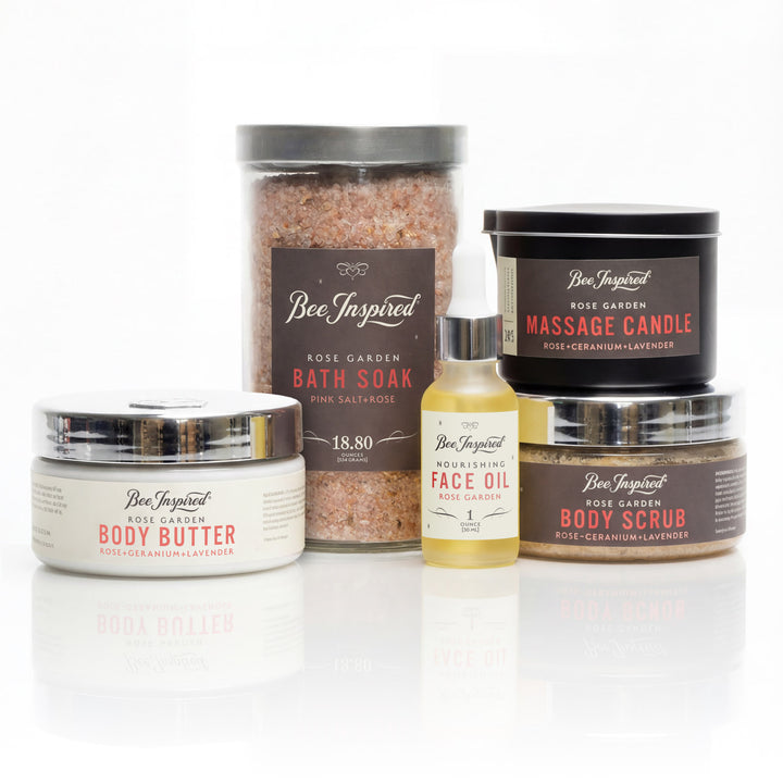 Collection of Bee Inspired beauty products including a face oil, massage candle, bath soak, body butter, and body scrub on a white background.