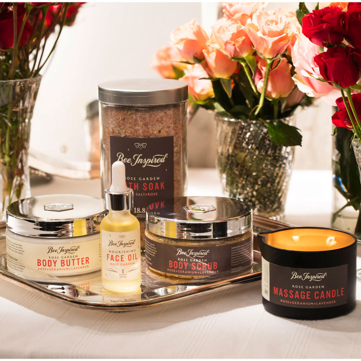 Collection of Bee Inspired beauty products including a jar, bottle, and candle with flowers in the background.