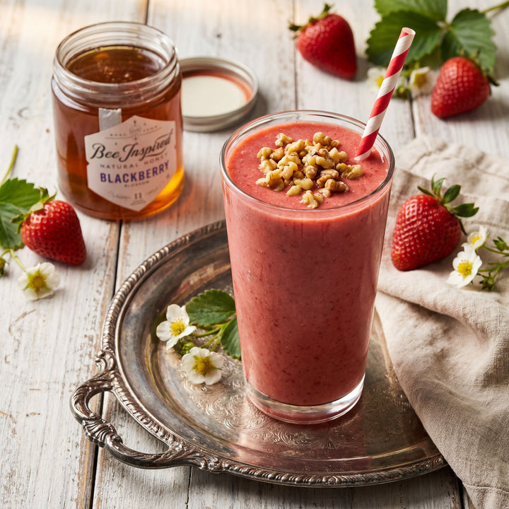 Strawberry smoothie with granola on a silver tray, surrounded by strawberries and a jar of blackberry jam.