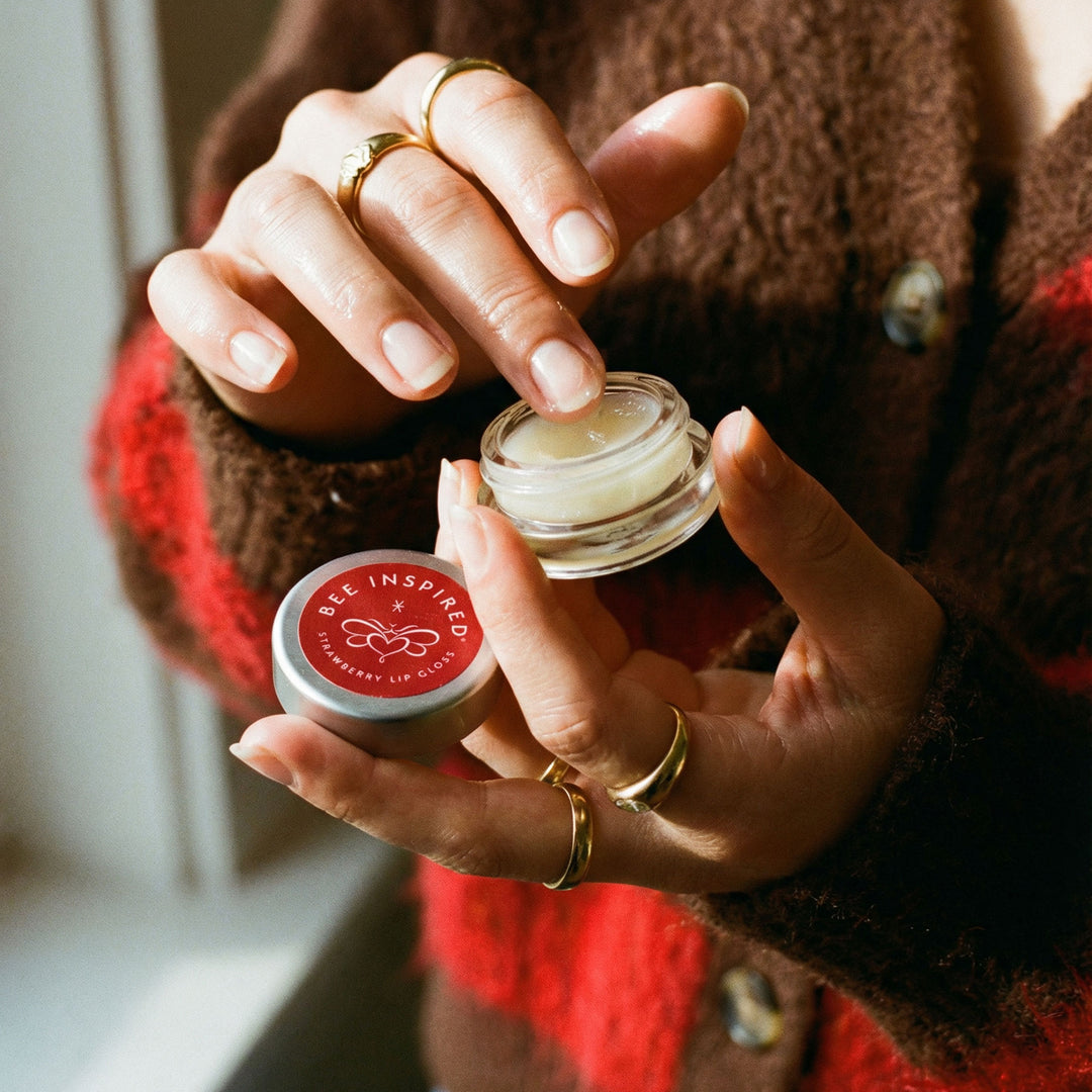 Person holding two lip balm containers with 'Bee Inspired' branding.