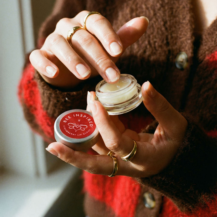 Person holding two lip balm containers with 'Bee Inspired' branding.