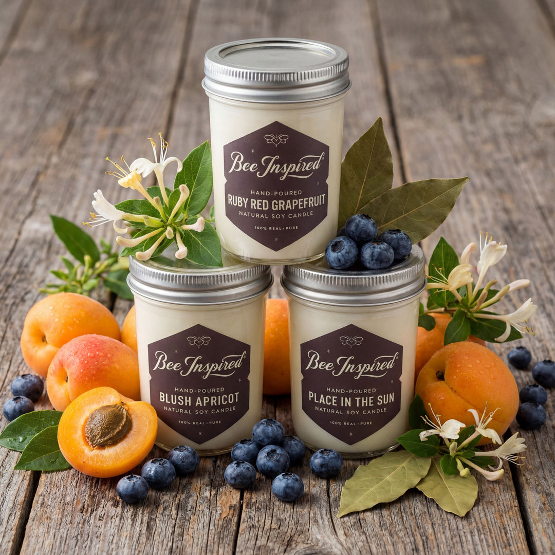 Three 'Bee Inspired' candles stacked on a wooden surface with fruits and flowers.