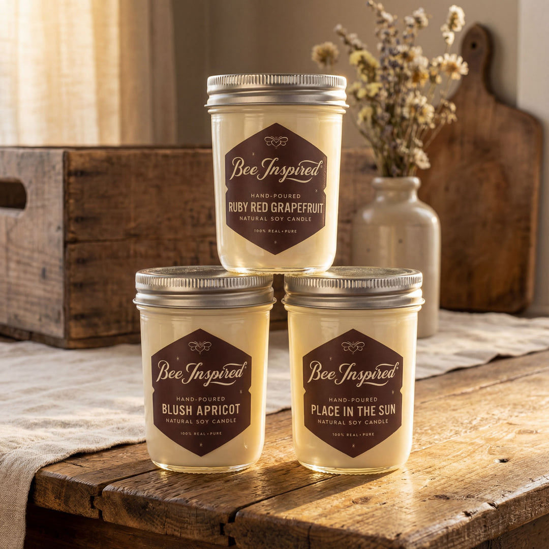 Three jars of 'Bee Inspired' candles on a wooden surface with a rustic background.