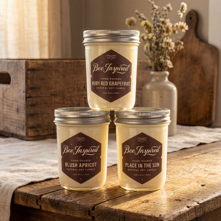 Three jars of 'Bee Inspired' candles on a wooden surface with a rustic background.