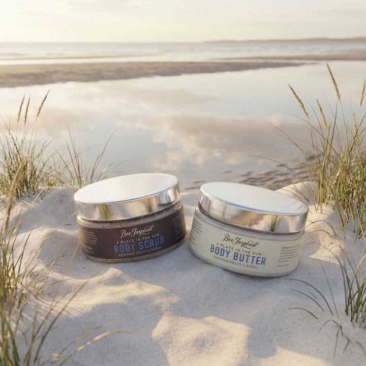 Two jars of Ben Elijah's Body Scrub and Body Butter on a sandy beach with grasses.