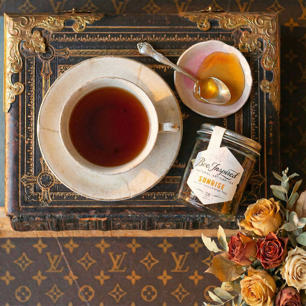Tea cup with saucer, jar of honey, and spoon on a decorative surface with flowers.