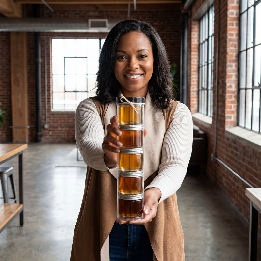 Woman holding a stack of glass jars filled with a amber liquid in an indoor setting.