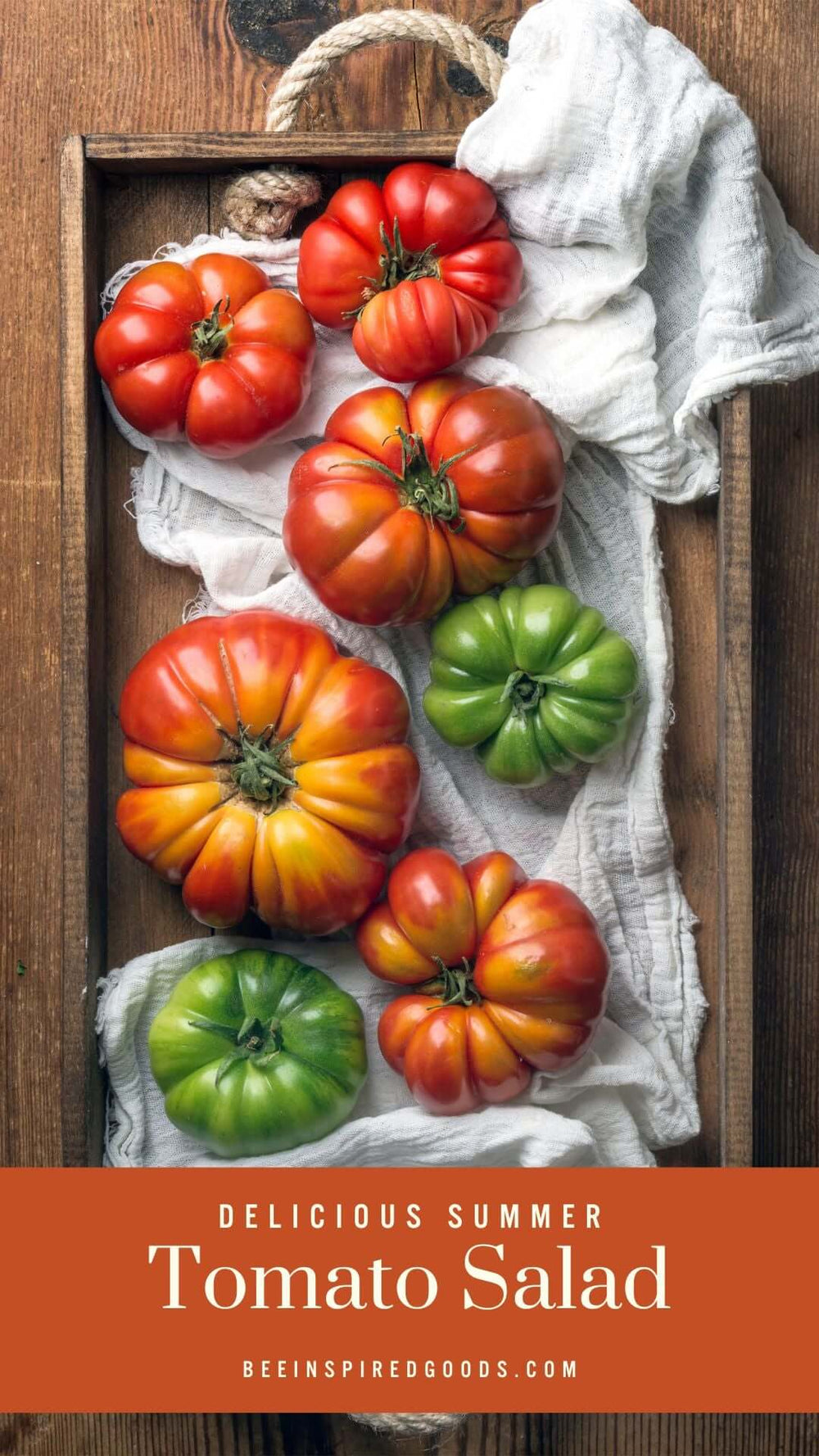 red and green tomatoes sit on a white cloth on a wooden table "Delicious Summer Tomato Salad beeinspiredgoods.com"