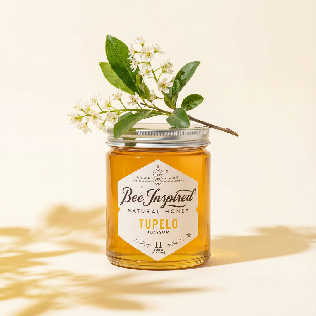Jar of 'Bee Inspired' Tupelo Blossom honey with a branch of flowers on a light background