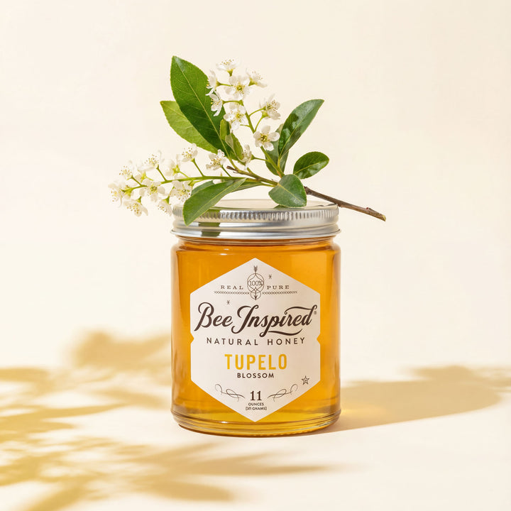 Jar of 'Bee Inspired' Tupelo Blossom honey with a branch of flowers on a light background