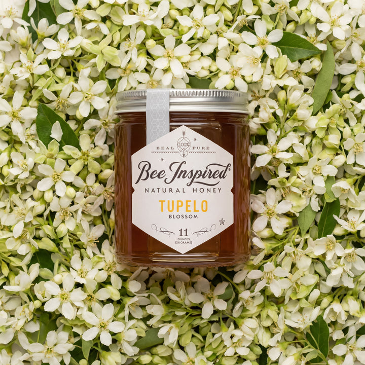 Jar of Bee Inspired Tupelo Blossom honey surrounded by white flowers