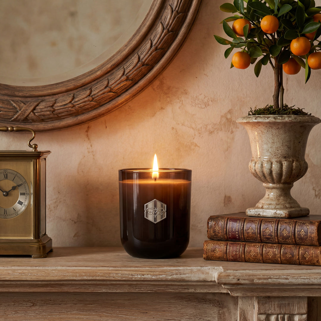 Candle burning on a wooden shelf with decorative items including a clock, books, and a potted plant.