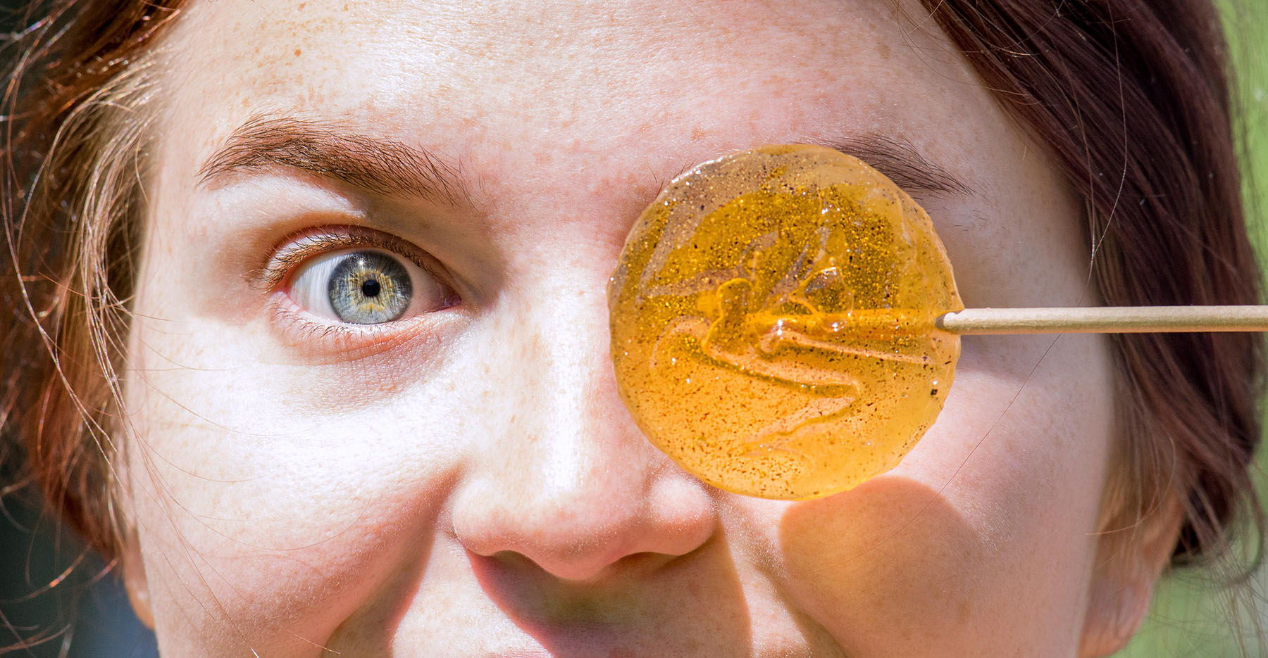 Woman holds lollipop in front of her eye like a monocle 