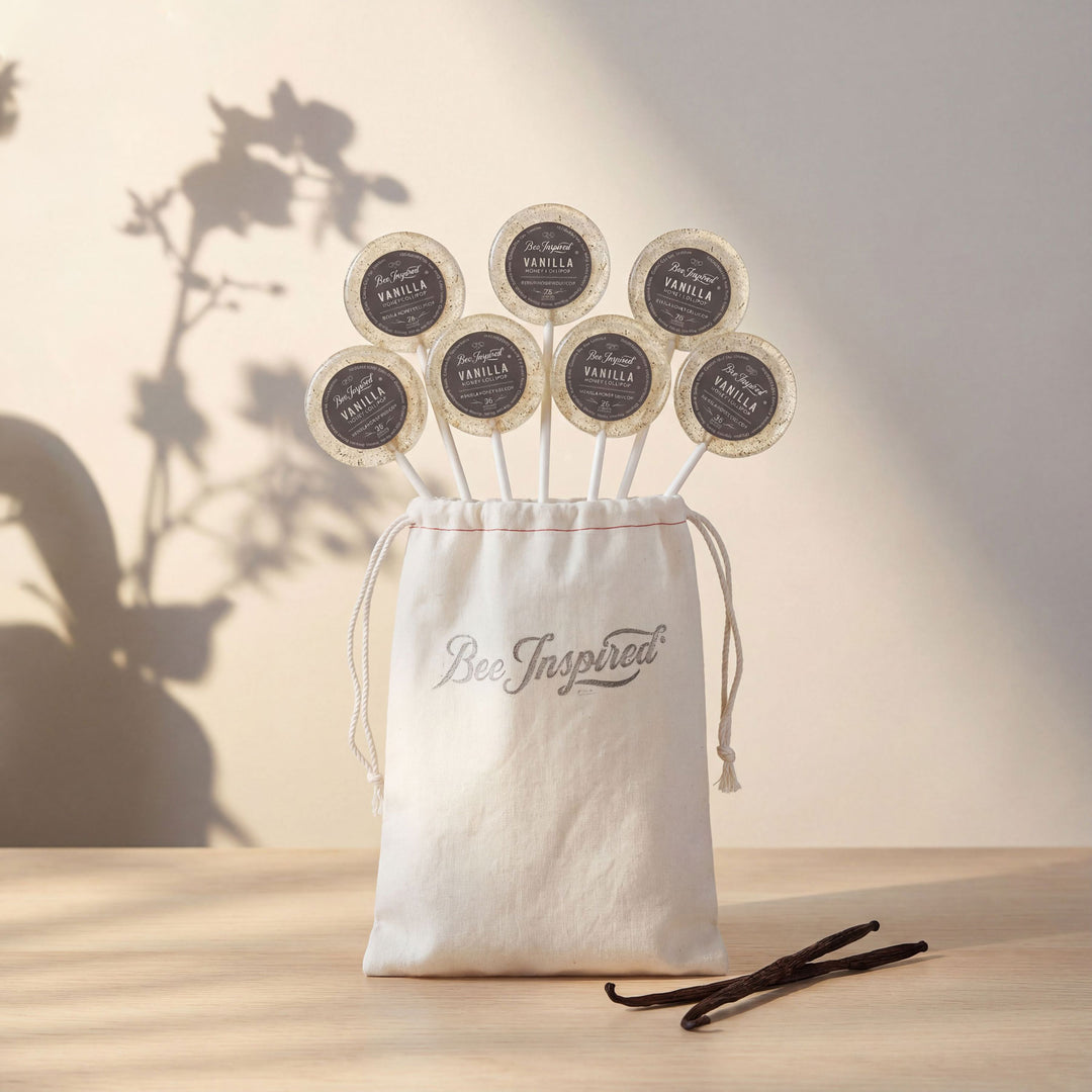 Vanilla pods with labels in a 'Bee Inspired' drawstring bag on a wooden surface.