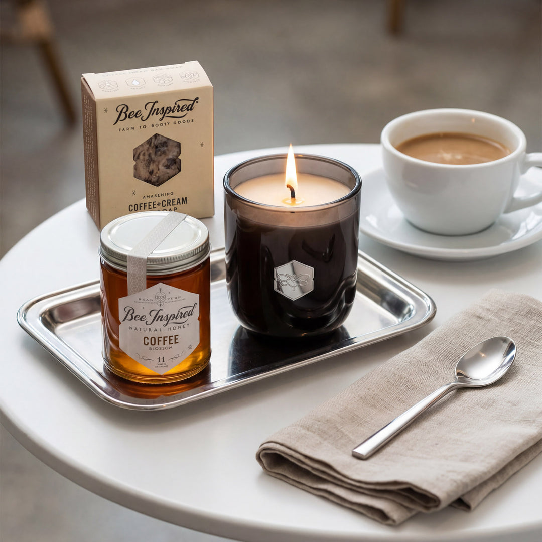 Candle, jar of honey, and coffee cup on a tray with a napkin and spoon on a table.