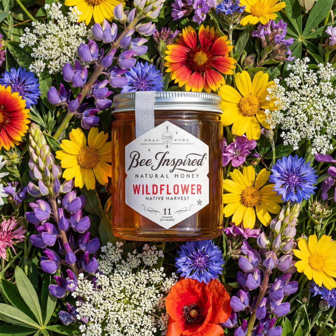 Jar of 'Bee Inspired' wildflower honey surrounded by a variety of colorful flowers