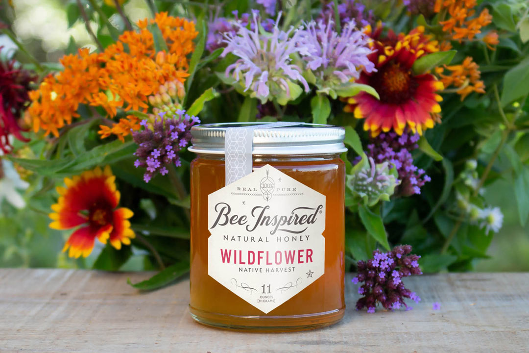 Wildflower honey by Bee Inspired Goods in front of a bouquet of wildflowers 