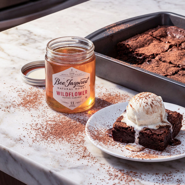 Jar of Bee Inspired Wildflower honey next to a plate of brownies with ice cream on a marble surface.