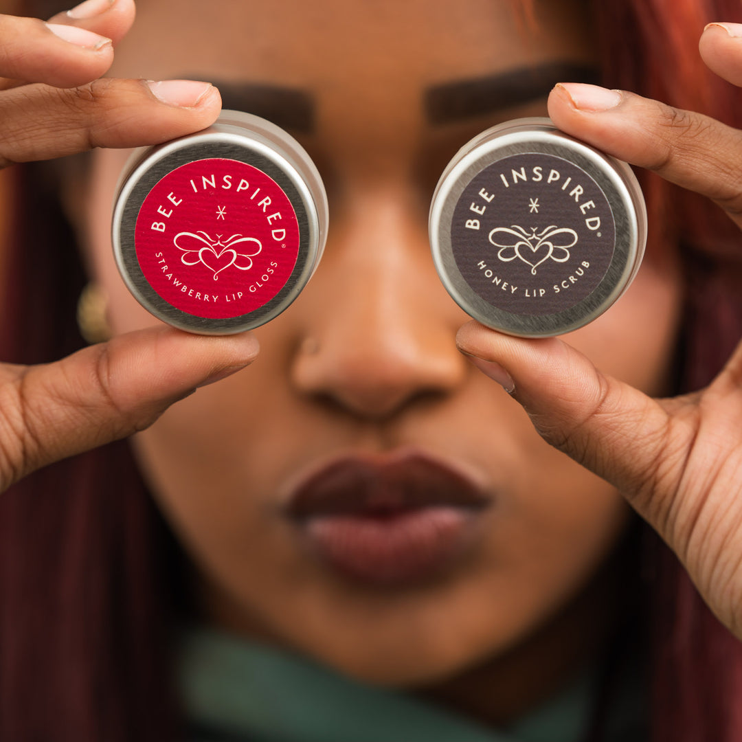 Woman holding strawberry lip gloss and honey lip scrub in front of her eyes 